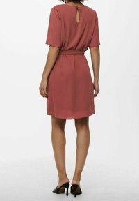 Vestido de manga corta, hasta la rodilla, en color rosa empolvado, que cuenta con una cintura ceñida con cinturón y un detalle de abertura en la espalda, fabricado con una tela suave.