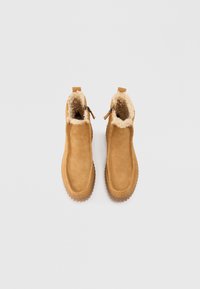Une paire de bottes d'hiver en daim beige avec des semelles en caoutchouc épaisses et une doublure en polaire crème, vues du dessus sur un fond blanc.