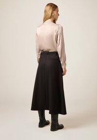 Silkeslen beige blus med lång ärm kombinerad med en svart, högmidjad A-linje kjol. Outfiten kompletteras med knähöga svarta stövlar.