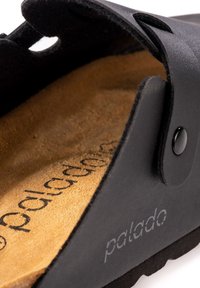 Svart slide-sandal med en texturerad, syntetisk ovandel. Har en brun, mjuk innersula och svarta detaljer, märkta med varumärket "palado."