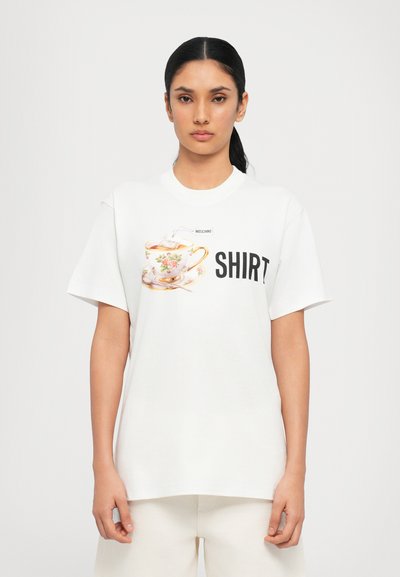 Fehér pamut póló, színes teáscsésze grafikával, virágmintákkal, alatta vastag fekete betűkkel a "SHIRT" felirattal.