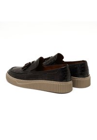 Zwarte loafer-schoenen van krokodillenleer met een gestructureerd leer, voorzien van een dikke beige rubberen zool en een decoratieve band op de wreef.