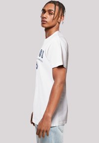 White cotton t-shirt with short sleeves, crew neck, and blue printed text and design on the front. Worn with light blue jeans.