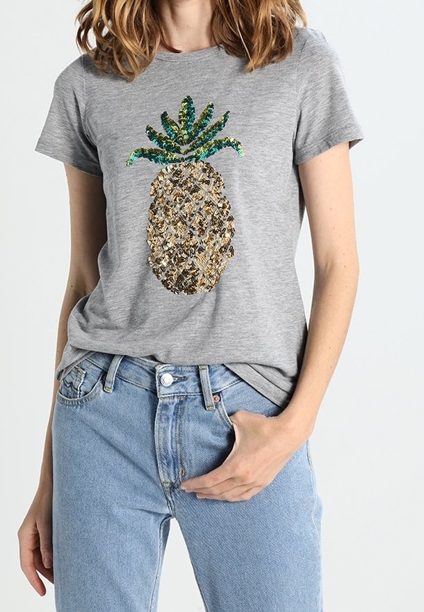 Camiseta gris de manga corta con un diseño de piña decorado con lentejuelas en dorado, verde y azul. Combinada con jeans de mezclilla azules.