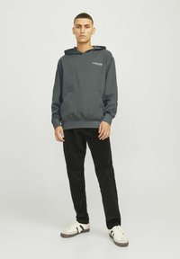 Donkergrijze hoodie met een voorzak en trekkoordkap, gecombineerd met zwarte corduroy broek en witte sneakers met zwarte accenten.