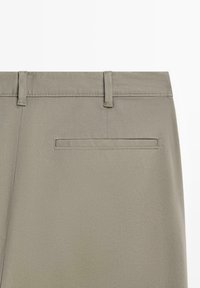 Dos d'un pantalon beige montrant des passants de ceinture et une poche passepoilée unique du côté droit.