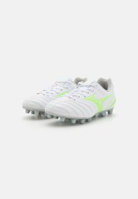 Vita fotbollsskor med grå detaljer, med en strukturerad yta, ljusgröna designelement och formade dobbar för grepp.