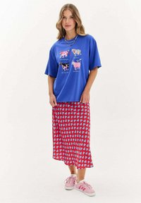 Modrá krátkosrstá tričková s potlačou kravy; červená sukňa s modrým srdcovým vzorom; ružové tenisky. Hladká textúra látky, neformálny dizajn.