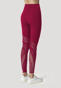 Leggings rossi con un motivo a rete testurizzato sui lati, con un design a vita alta. Abbinati a sneakers bianche.