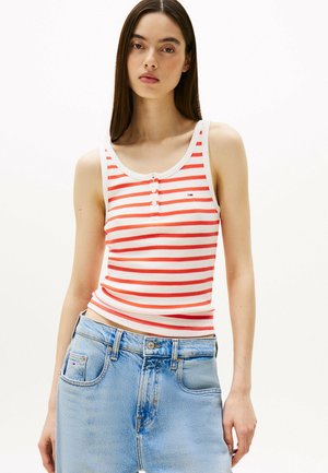 Top in tessuto a righe rosse e bianche con scollatura a giro e dettaglio con bottoni, abbinato a jeans azzurri a vita alta. Texture del tessuto liscia.