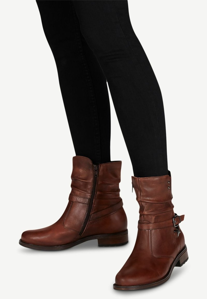 Bruna läderankelboots med en slouchad design, sidodragkedja, dekorativa spännen och medelhöga klackar.