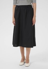 Falda negra hasta la rodilla con una cinturilla elástica, hecha de una tela suave, presenta un diseño simple y fluido. Combinada con zapatos beige.