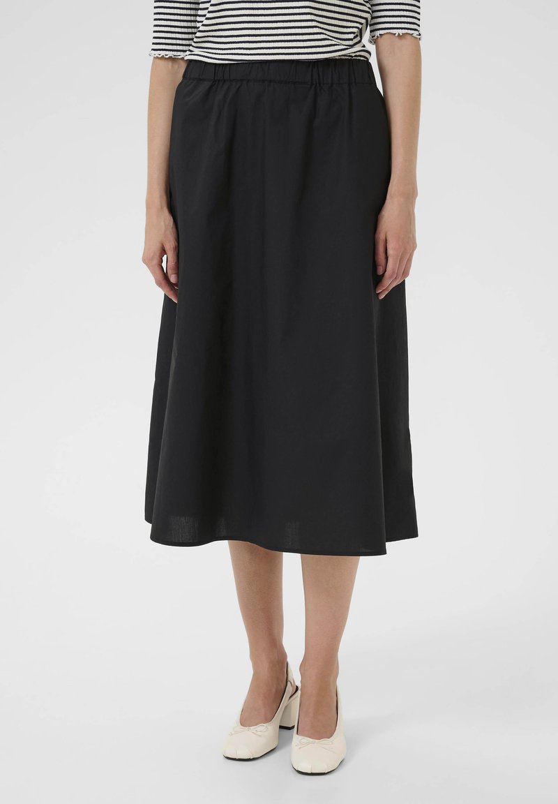 Falda negra hasta la rodilla con una cinturilla elástica, hecha de una tela suave, presenta un diseño simple y fluido. Combinada con zapatos beige.