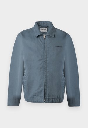 Veste zippée bleu pour homme avec col et poches latérales, arborant un petit logo Carhartt noir sur la poitrine gauche.