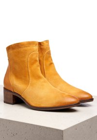 Hnědé kožené kotníkové boty s hladkým povrchem, nízkým polstrovaným podpatkem a zaoblenou špičkou. Výrazné boční švy a elegantní, minimalistický design.