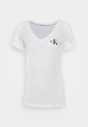 Valkoinen lyhythihainen V-pääntie T-paita, jossa musta "CK Calvin Klein Jeans" -logo vasemmassa rinnassa, esitettynä yksinkertaisella taustalla.
