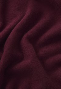 Tissu bordeaux avec une surface douce et texturée, présentant de légères plis et une couleur riche et profonde, adapté à diverses applications textiles.