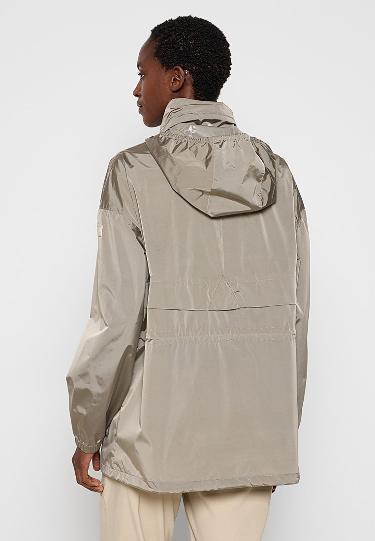 Giacca leggera e impermeabile in beige con cappuccio. Presenta una superficie liscia e lucida e una ventola posteriore per la traspirabilità. Design semplice.