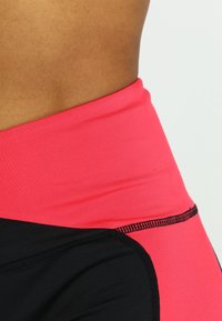Leggings a vita alta di colore nero con un elastico fucsia, caratterizzati da una texture liscia e dettagli di cucitura a contrasto lungo le cuciture.