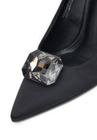 Pantof high-heel cu vârful ascuțit, de culoare neagră, cu o mare gemă pătrată transparentă, tăiată, amplasată în față.