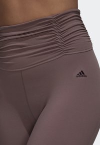 Højtaljede træningsleggings i en dæmpet mauve farve, med en sammensamlet talje og et lille sort adidas-logo ved hoften.