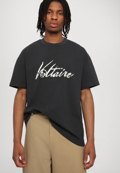 Schwarzes Baumwoll-T-Shirt mit einem weißen Grafikdruck des Wortes "Voltaire" und einem Totenkopf-Detail. Lockere Passform mit kurzen Ärmeln.