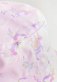 Chapeau seau violet sur un fond rose, arborant un motif de licornes et de designs floraux. Fabriqué en tissu léger avec une couture. 