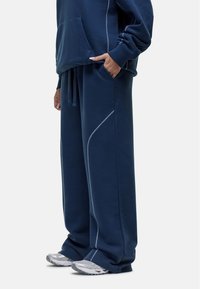 Marineblauwe sweatshirt met een voorzak, gecombineerd met wijde broek met witte stiksels en een koord in de taille.