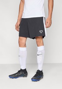 Fekete sportnadrág fehér oldalsávokkal és Nike logóval, fehér zoknival fekete részletekkel, valamint fekete stoplis cipőkkel kék díszítéssel.