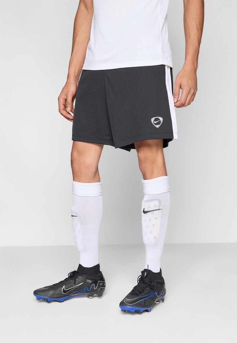 Fekete sportnadrág fehér oldalsávokkal és Nike logóval, fehér zoknival fekete részletekkel, valamint fekete stoplis cipőkkel kék díszítéssel.