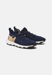 Zapatillas de malla color marino con acentos en beige, que cuentan con un cuello acolchado, cordones elásticos y una entresuela blanca. Suela de caucho para mayor agarre.