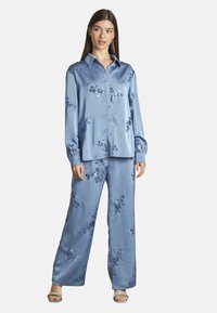 Lichtblauwe satijnen pyjama set met een lange mouw, knoopjesoverhemd en brede broekspijpen, versierd met bloemenborduursels en pailletaccenten.