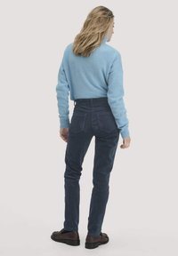 Lichtblauwe trui, nauwsluitende marineblauwe corduroy broek en donkere schoenen. Zichtbare stiksels en vijf-pocketdesign op de broek; de trui heeft ribbelboorden.