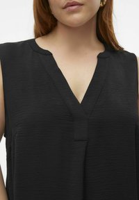 Top noir sans manches avec un décolleté en V, en tissu texturé, et une coupe décontractée. Détails de couture subtils le long du décolleté et de l'ourlet.