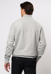 Szürke kapucnis pulcsi, puha anyagból készült. Ribbed mandzsettákkal és hem-el rendelkezik, a sleve-n pedig egy kis színes logó található.
