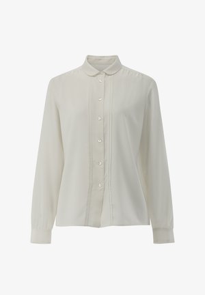 Blusa bianca a maniche lunghe con bottoni sul davanti, colletto piccolo a punta e sottili pieghe verticali ai lati dei bottoni.