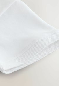 Hvid bomuldsstof med en ribbet tekstur i kanten, der viser en glat, ren finish og subtile syninger.