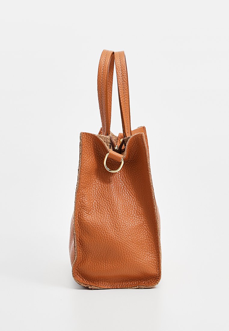Braune Leder-Tote mit strukturiertem Finish, elongated Form, zwei Griffen und einem goldenen runden Akzent am Eingang.