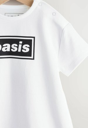 Vit bomull t-shirt med en svart rektangulär tryck som står "basis." Har rund halsringning, korta ärmar och två tryckknappar på axeln.