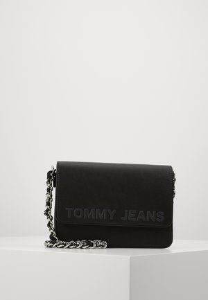 Black Tommy Jeans crossbody bag with flap closure and silver-and-black chain strap on white pedestal against a plain background.