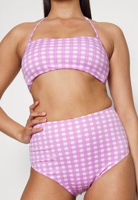 Conjunto de bikini em duas peças com um padrão de quadrados rosa e branco. O top possui um design sem alças, e a parte de baixo de cintura alta oferece cobertura total.