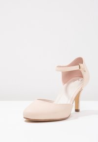 Beżowe sandały na wysokim obcasie z teksturowanej skóry, o okrągłym czubku i pasku wokół kostki. Wąski obcas i wyściełana wkładka.