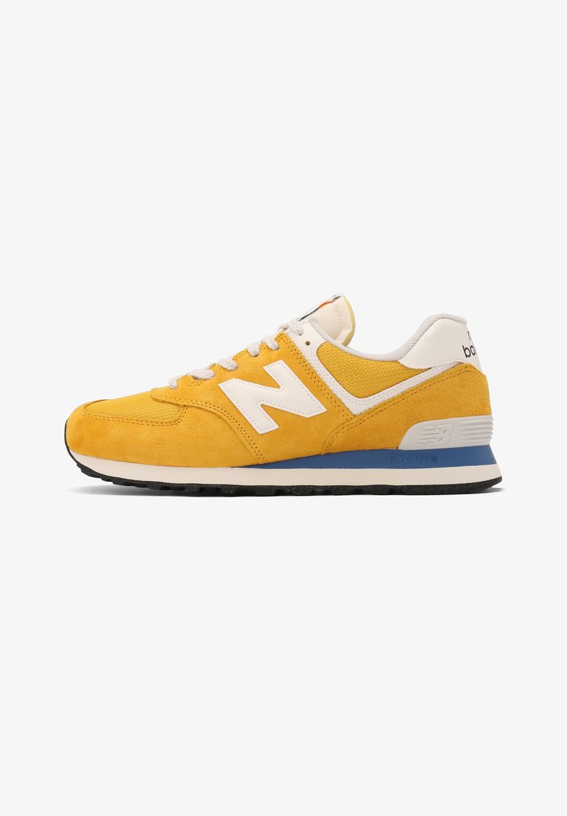 Baskets New Balance jaunes avec lacets blancs, logo blanc, semelle bleue et blanche, et semelle extérieure noire, vues de côté extérieur.