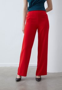 Red wide-leg trousers with a smooth texture, featuring two side pockets and a high-waisted design, paired with black heels.