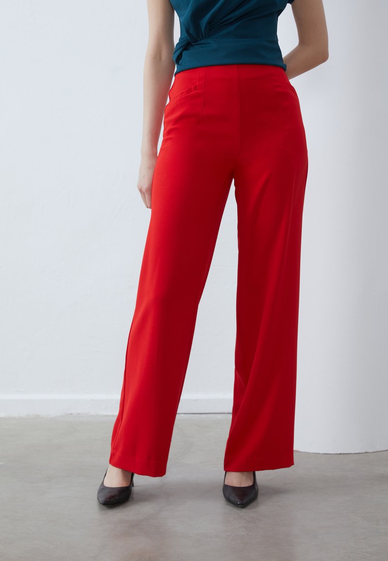 Red wide-leg trousers with a smooth texture, featuring two side pockets and a high-waisted design, paired with black heels.