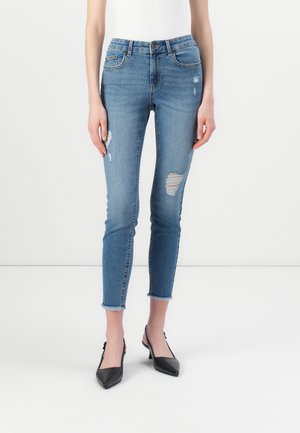 Fitted blue jeans with distressed details, mid-rise waist, ankle-length, frayed hem, and classic five-pocket design. Pairing with black heels.