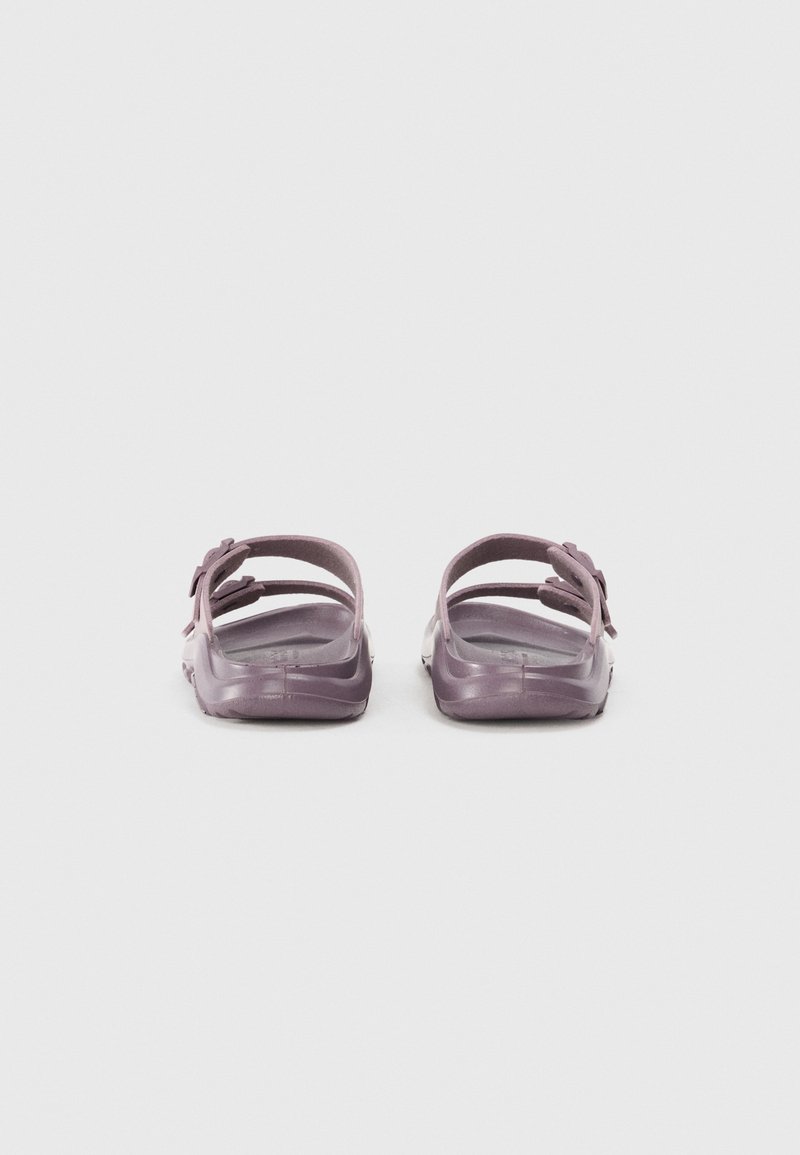 Sandales en plastique violet avec plusieurs sangles, design ouvert à l'arrière, texture lisse et un petit nœud décoratif sur chaque chaussure.