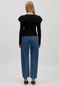 Black ribbed long-sleeve top with ruffled shoulder accents paired with high-waisted light blue straight-leg jeans and black heels.