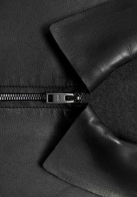 Abbigliamento in pelle nera con chiusura a zip frontale, caratterizzato da una texture liscia e cuciture minime, accentuato da un colletto ripiegato.