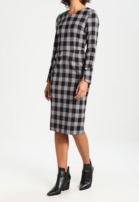 Svart och vit rutigt klänning med långa ärmar, figursydd silhuett, knä-lång, med rund halsringning och guldknappaccent på ärmarna.